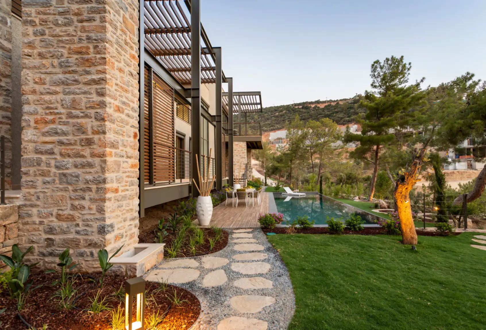 Modern Mediterranean stone estate with pergola terraces, infinity pool and landscaped grounds at dusk